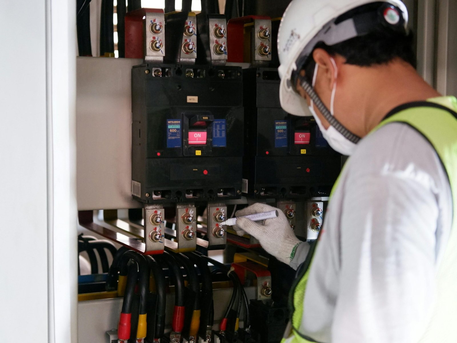 service-1 Technician wearing safety gear inspecting electrical panels in an industrial setting.